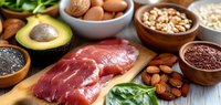 Assortment of healthy protein sources with raw meat, avocado, eggs, nuts, seeds and greens on wooden background.