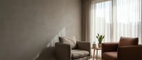 Modern minimalist living room interior with brown leather armchairs, concrete wall, sheer curtains and natural sunlight for contemporary home design.