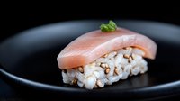 Fresh tuna nigiri sushi with rice garnished with micro greens served on black ceramic plate against dark background, traditional Japanese cuisine.