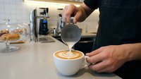 Skilled barista pouring steamed milk into a latte cup, creating intricate latte art in a modern coffee shop setting.