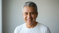 Smiling mature Hispanic man with gray hair wearing white t-shirt against neutral background. Professional headshot for business and lifestyle content.