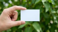Hand holding blank white business card against green foliage background for branding mockup and corporate identity design templates.