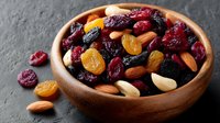 Wooden bowl filled with mixed dried fruits and nuts including cranberries, raisins, almonds and cashews on dark slate background for healthy snacking.