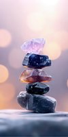 Balanced stack of healing crystals and mineral stones in purple and dark tones against soft bokeh background, creating zen and spiritual atmosphere.