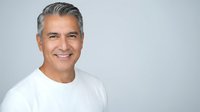 Confident mature Hispanic man with gray hair smiling warmly in white t-shirt against neutral background for lifestyle and wellness content.