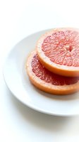 Fresh grapefruit slices arranged on white plate, showcasing vibrant pink citrus flesh and natural texture for food photography, healthy eating, and culinary content.