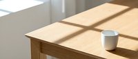Wooden desk with white ceramic cup and natural sunlight casting shadows through window, suitable for workspace and office design projects.
