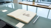 Open notebook with hello written in elegant calligraphy on a glass desk beside a silver pen in a modern office setting.