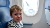 Toddler boy with light brown hair sitting by airplane window during flight, wearing striped shirt, travel and aviation concept.