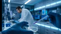 Scientist in laboratory conducting research with pipette and petri dish in modern facility with blue lighting.