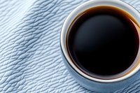 Cup of black coffee in ceramic mug on textured light blue surface viewed from above, with dramatic side lighting creating contrast and depth. Minimalist food photography.