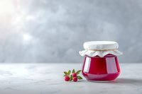 Homemade raspberry jam in glass jar with fresh berries on light marble table against gray background, perfect for food packaging design.