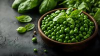 Fresh green peas in wooden bowl with basil leaves on dark background. Natural organic vegetables with vibrant color and rustic presentation for food styling.