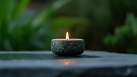 Glowing tea light candle in dark stone holder against blurred green background creates peaceful zen atmosphere for spa and meditation settings.