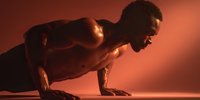 Athletic man performing push-up exercise in dramatic red lighting showcasing strength training and fitness dedication for workout motivation content.