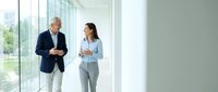 Professional business colleagues walking together in modern office corridor discussing strategy and collaboration during corporate meeting.
