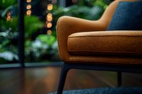 Modern brown armchair with textured fabric upholstery and black metal legs against blurred bokeh lights and green plants background, cozy interior design element.