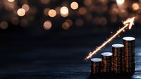 Glowing arrow rises over stacks of coins showing financial growth and success against dark background with golden bokeh lights and copy space.