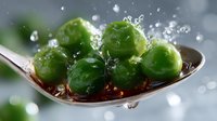 Fresh green Brussels sprouts on metal spoon with water drops and splashes in dramatic lighting, macro food photography for healthy eating concept.