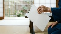 Mature man with medium skin tone in dark blazer holding blank white paper sheet indoors, suitable for business communication, document presentation, or corporate messaging concepts.