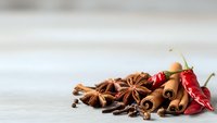 Aromatic spices including star anise, cinnamon sticks, cloves and dried chili peppers arranged on rustic wooden surface for cooking and seasoning.