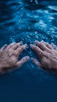 Mature male hands immersed in rippling blue water with floating droplets, conveying refreshment, wellness, and natural hydration for spa, health, and lifestyle concepts.