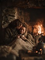 Cozy couple sharing intimate moment by fireplace wrapped in warm blankets during winter evening at home creating romantic atmosphere for relaxation.