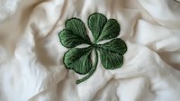 Green four-leaf clover embroidered on white fabric with delicate stitching detail and textured pattern creates lucky charm symbol for St Patrick's Day celebrations.