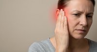 Middle-aged Caucasian woman experiencing severe ear pain holding hand to inflamed ear showing symptoms of infection or hearing problems for medical content.