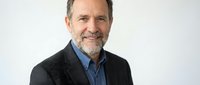 Middle-aged Caucasian man with gray beard wearing dark blazer and blue shirt, smiling at camera against white background for corporate or professional headshot use.