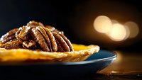 Caramelized pecan nuts on dark plate with golden bokeh background, close up macro shot highlighting texture and glossy surface of nuts in warm lighting.