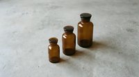 Three amber glass bottles with cork stoppers arranged in ascending size order on a concrete surface, suitable for pharmaceutical, cosmetic, essential oil, and apothecary product packaging designs.