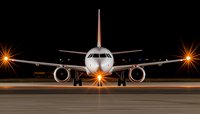 Commercial passenger aircraft on runway at night with dramatic lighting from landing lights and orange airport illumination creating atmospheric scene.