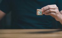 Hand holding wooden cube with house and percentage symbol representing mortgage rates, real estate investment, property financing concepts.