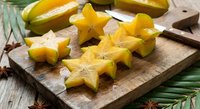 Fresh star fruit slices on wooden cutting board with knife, tropical carambola ready for healthy snacking and culinary preparation.