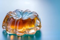 Amber-colored jelly dessert in decorative glass mold shape against blue background with soft lighting and reflective surface creates elegant culinary composition.