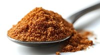 Brown muscovado sugar heap on metal spoon against white background, close up view showing natural raw sugar crystals and rich caramel color texture.