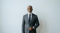 Mature African American male executive in formal gray blazer and navy tie standing against white background for corporate and business use.
