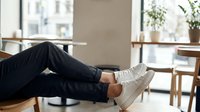 Person in dark jeans and white sneakers relaxing with feet up on modern cafe table. Casual lifestyle moment in bright contemporary restaurant interior.