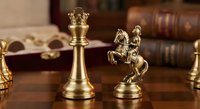 Luxury brass chess pieces king and knight on wooden board with vintage books creating elegant strategic game atmosphere for sophisticated interior design.