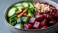 Fresh beet and cucumber bowl with almonds, pine nuts and herbs in white ceramic bowl, healthy vegetarian lunch macro photography on gray background.