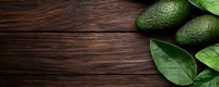 Fresh ripe avocados and green leaves arranged on dark wooden rustic table background with copy space, top view panoramic composition for food banner.