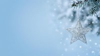 Decorative silver star ornament hanging from evergreen branch against soft blue sky with falling snow and bokeh lights, suitable for holiday and seasonal marketing.
