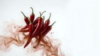 Fresh red chili peppers with spice powder explosion on white background, capturing heat and bold flavor for food and culinary concepts.