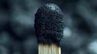 Charcoal makeup brush with black bristles and wooden handle on blurred background for cosmetic application and beauty routines.