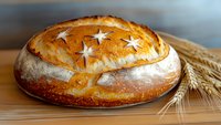 Fresh baked artisan sourdough bread with star pattern scored on golden brown crust, served on wooden surface with decorative wheat stalks.