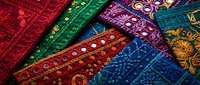 Colorful traditional embroidered textile fabrics with intricate patterns and golden details arranged in overlapping layers for cultural design projects.