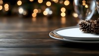 Festive table setting with white plate, pine cone and blurred bokeh lights in background, creating warm holiday atmosphere on dark wooden surface.