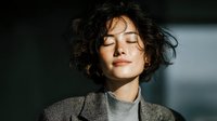 Young woman with curly hair enjoying peaceful moment with eyes closed in natural sunlight for wellness and mindfulness concepts.