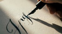 Calligraphy pen writing elegant script lettering on white paper with natural sunlight casting shadows, suitable for art, design, and educational projects.